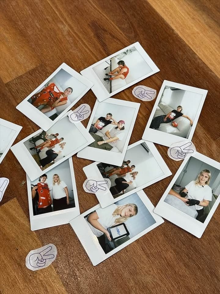 Polaroids scattered on a table of three different women smiling in various positions, as well as a number of tattoo stencils