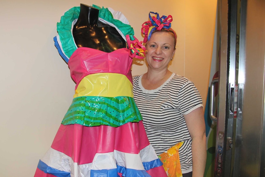 A woman stands in front of a mannequin in a colourful dress