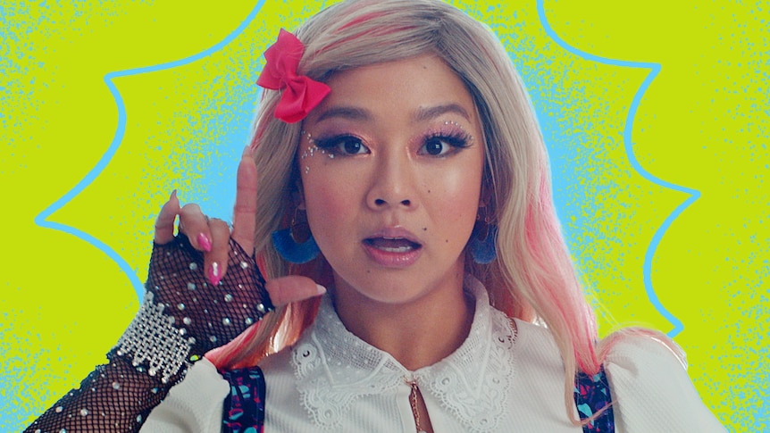 Actress Stephanie Hsu dressed up as a k-pop star, making a loser hand signal, in a still from her new movie Joy Ride.