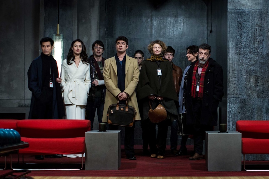 A scene from the movie The Translators with a group of people standing together in a grey room