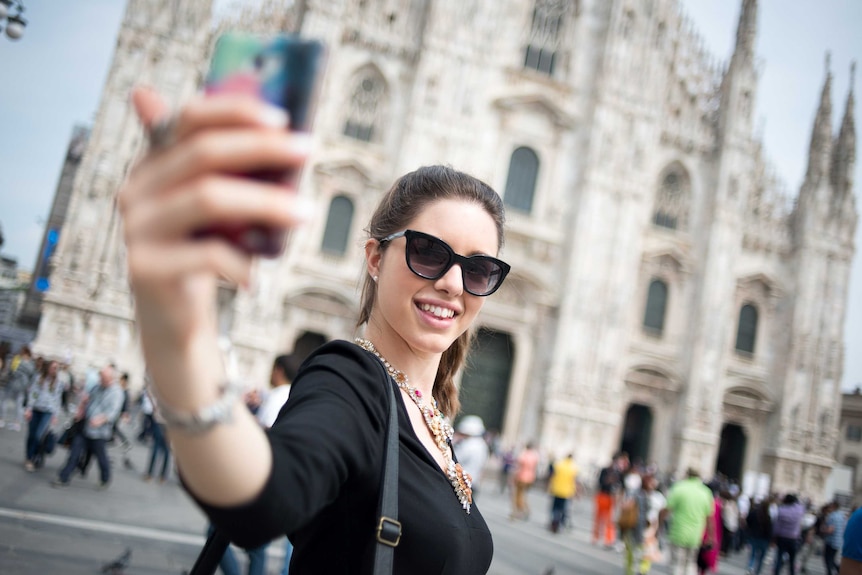 A young woman takes a selfie with her phone outside the Duomo Cathedral in Milan.