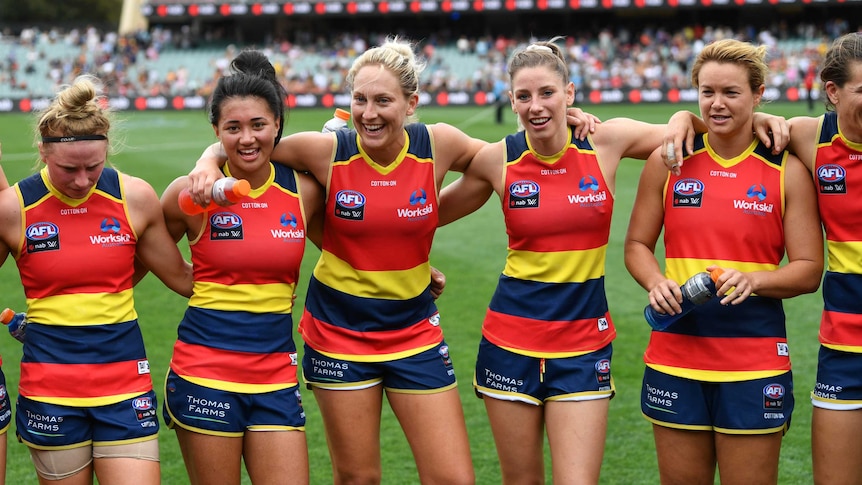 Five Crows players stand arm in arm, smiling and celebrating their win.