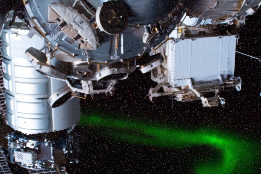 The Northern lights are shining green under parts of the International Space Station