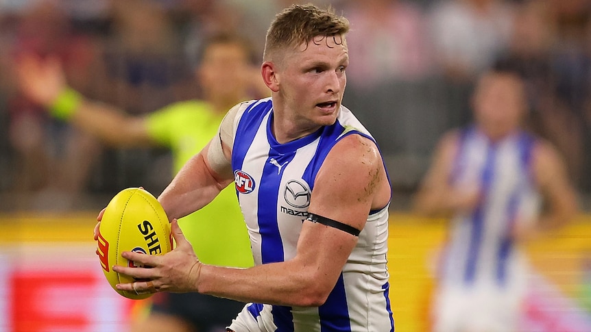 A North Melbourne AFL player holds the ball in two hands in a 2023 match.