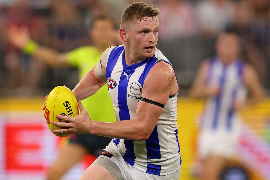 A North Melbourne AFL player holds the ball in two hands in a 2023 match.