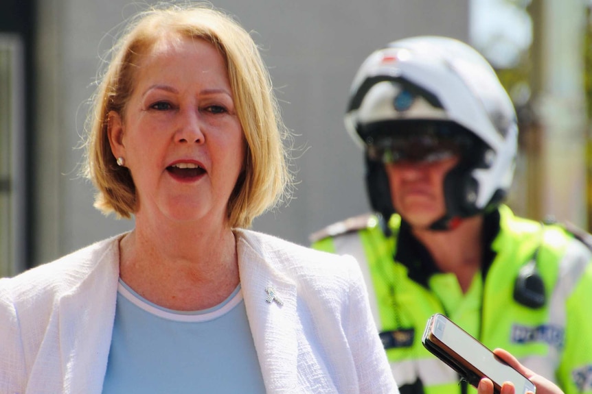 A mid-shot of WA Police Minister Michelle Roberts wearing a white jacket and blue top with a police officer behind her.