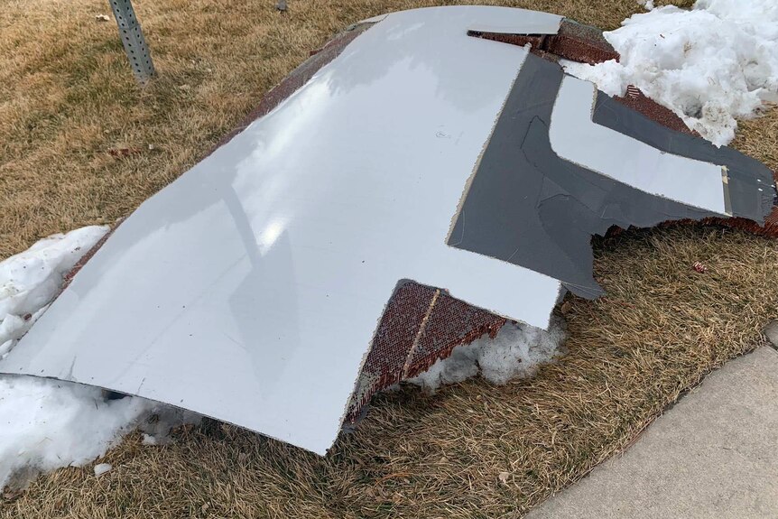 A white piece of aircraft debris sits on grass next to snow.