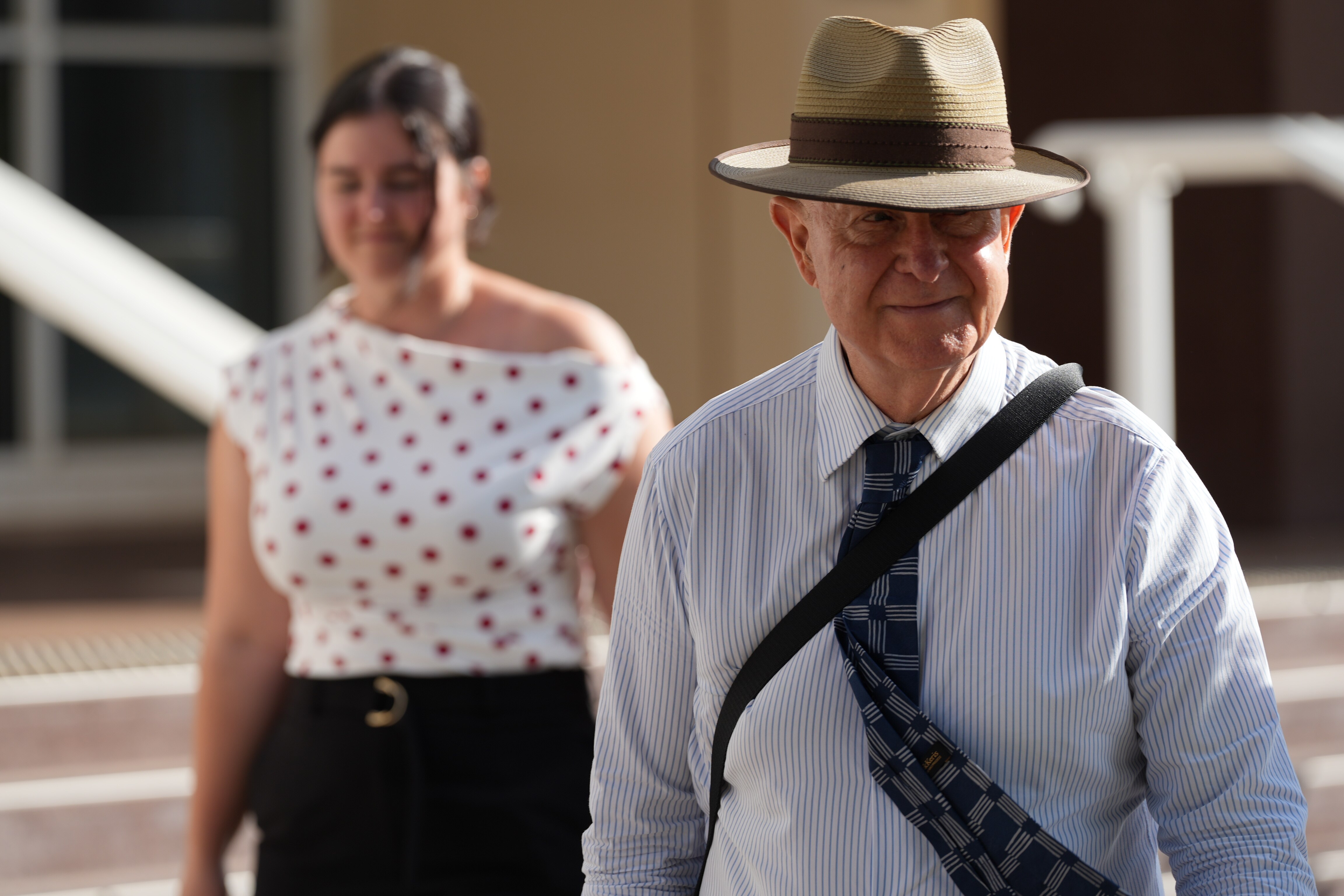 Un hombre con camisa abotonada, corbata y sombrero sale de la sala.