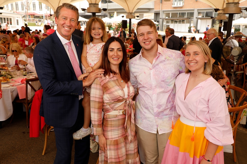 A family of two adult children and one young girl and a man and woman stand in a crowded marquee