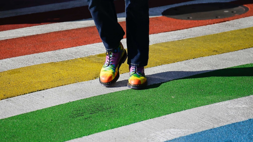 A person wearing rainbow-coloured boots walks across a rainbow-painted road