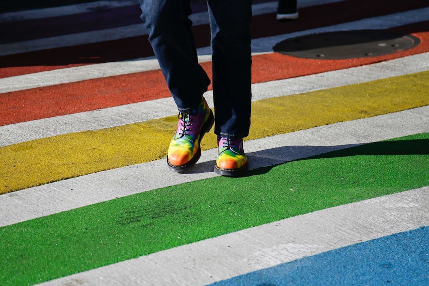 A person wearing rainbow-coloured boots walks across a rainbow-painted road