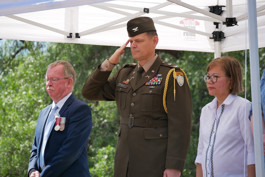 three people standing to attention under a tent