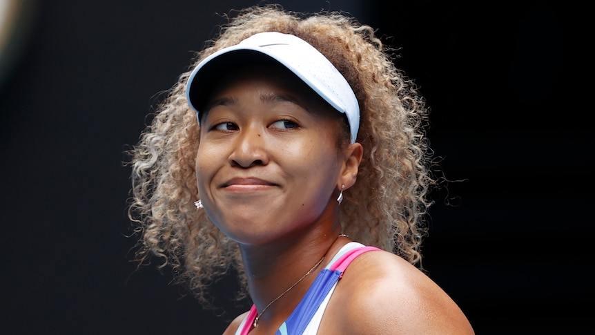Tennis player Naomi Osaka, wearing a white visor, smiles during a match.