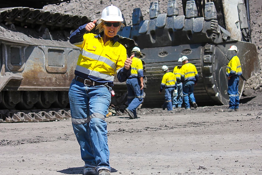 Leanne Drew in high-vis clothing in front of massive earth-moving equipment on a mine site