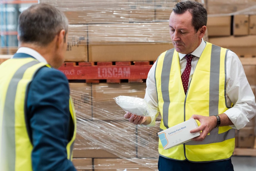 Mark McGowan and Roger Cook in high-viz vests in a warehouse looking at boxes of surgical masks.