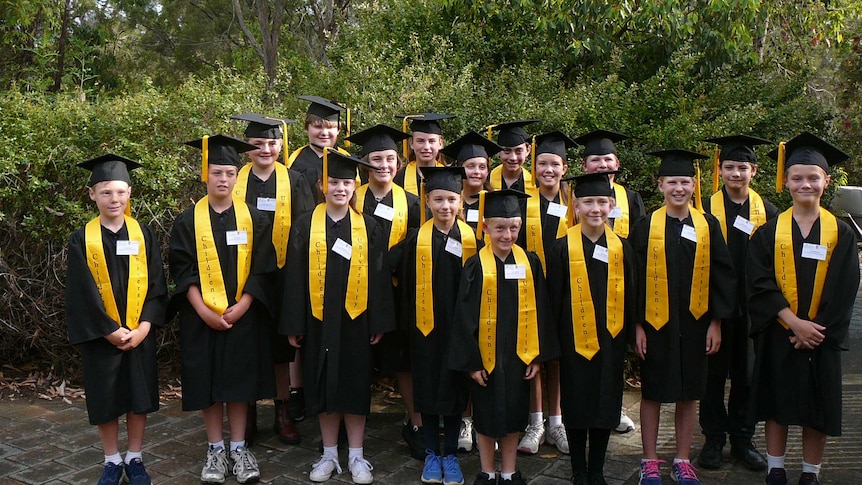 A group of children wearing black graduation robes and mortar-boards with yellow tassels.