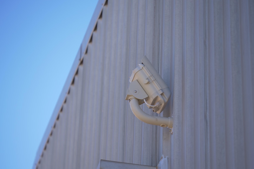 A white camera attached to a wall, aiming up.