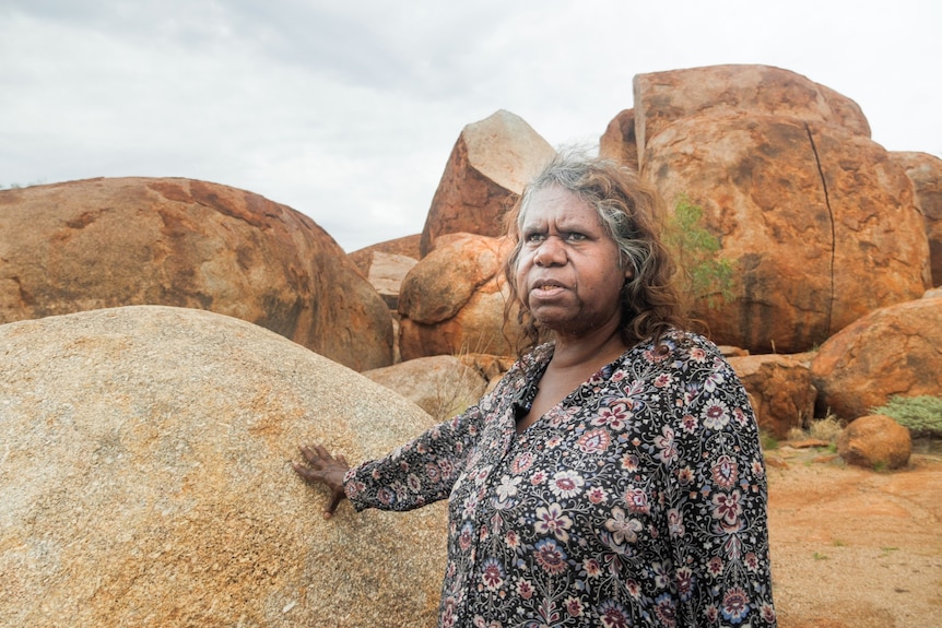 A woman stands near a rock