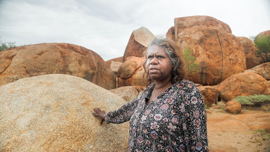 A woman stands near a rock