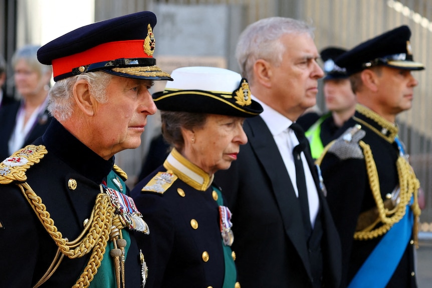 查尔斯国王、安妮公主和爱德华王子穿着制服盯着前方，旁边是穿着西装的安德鲁王子