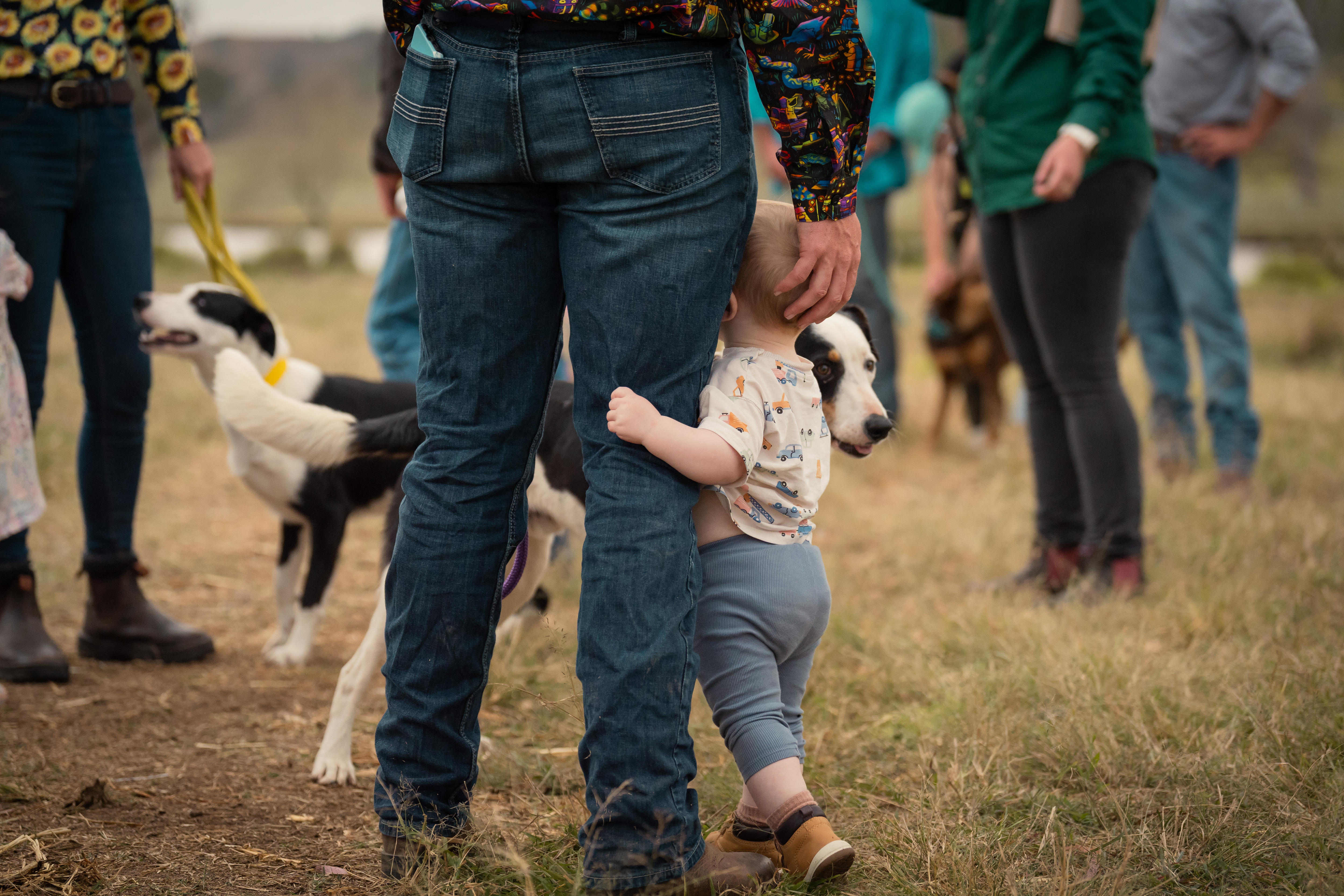 A baby holds the right leg of his dad.