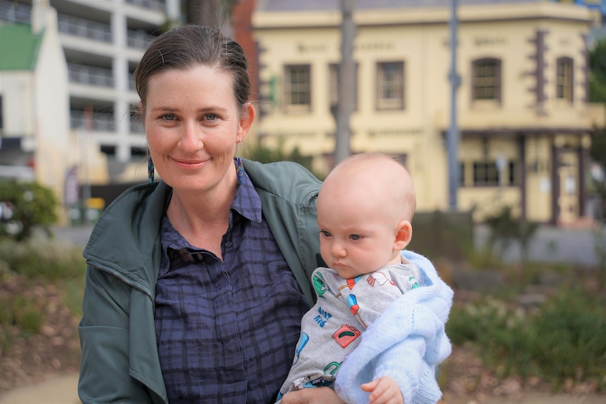 A woman holding a baby looks at the camera