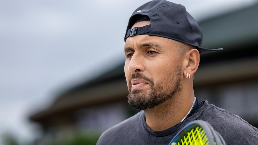 A pensive Nick Kyrgios looks down as he stands on a practice court with his racquet.