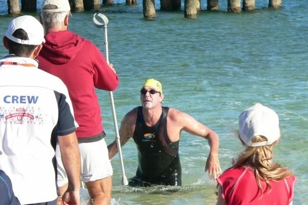 Athlete who lost a limb competing in ocean swim comes to shoreline with assistant holding walking aid