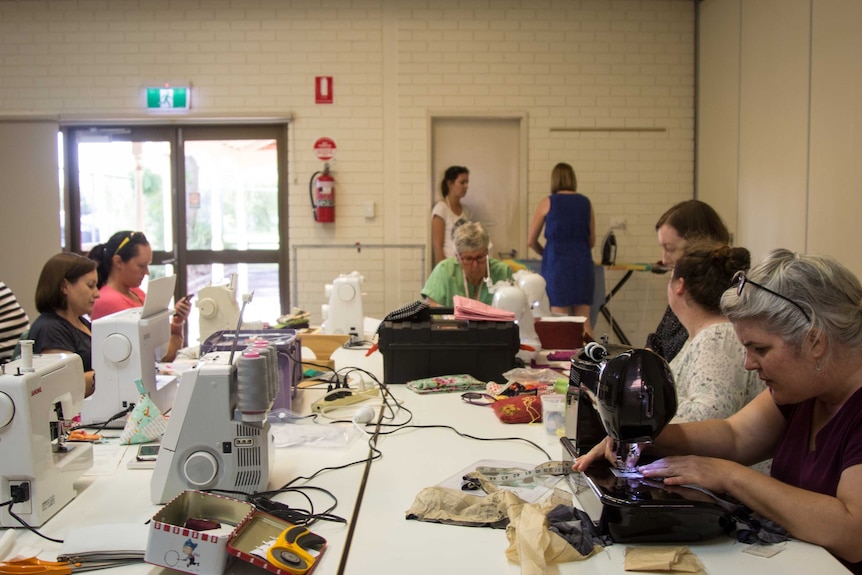 Group of women sit around a table sewing.