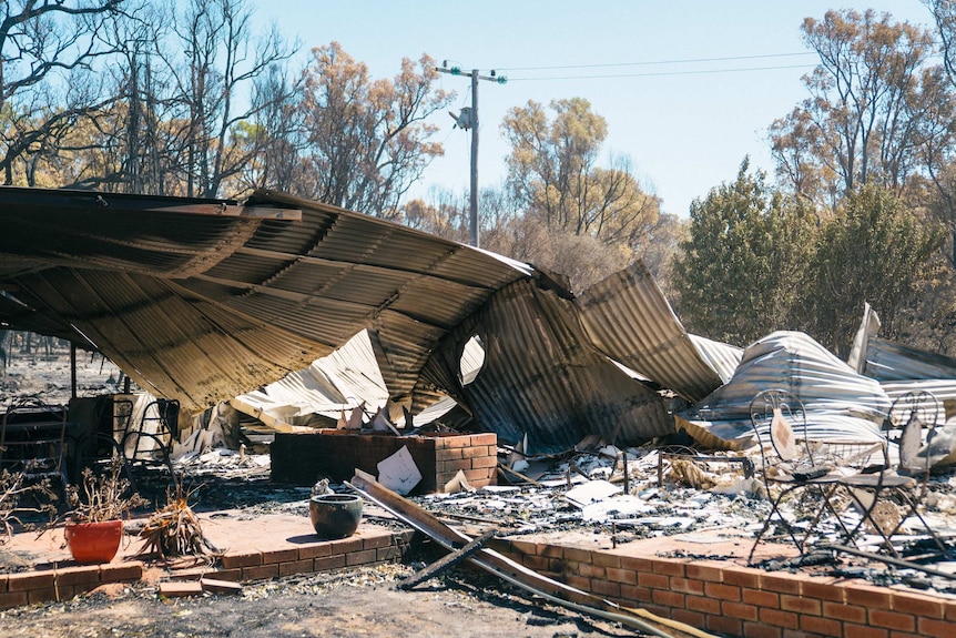 Corrugated iron lies on the ground, burnt metal chairs sit on bricks.