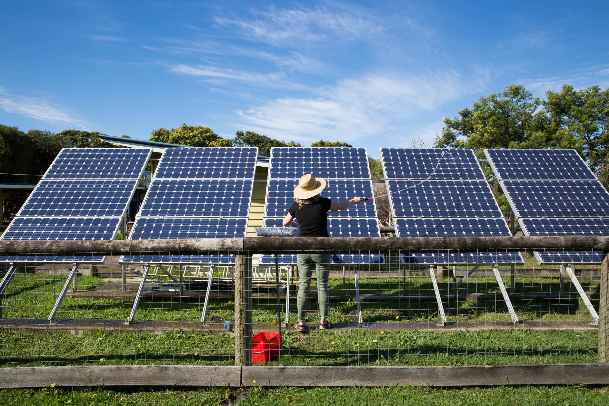 Una mujer arroja agua de una manguera a una vaina de paneles solares.