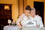 Two women wearing white and holding a 'just married' sign.