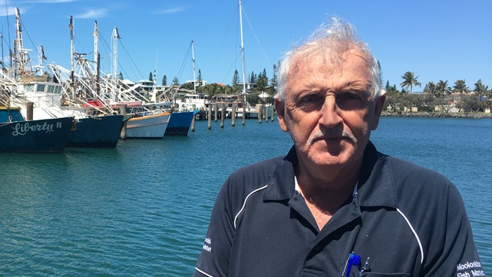 A man standing at a pier with prawn trawlers in the background