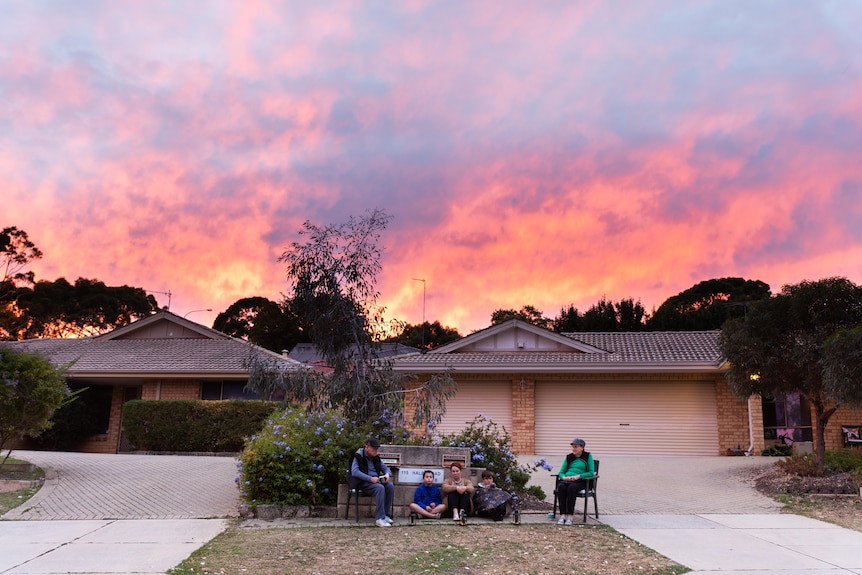 A beautiful sunset overhead a family sitting on their driveway.