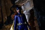 Batgirl stands solemnly by a stone pillar, casting a shadow onto it.