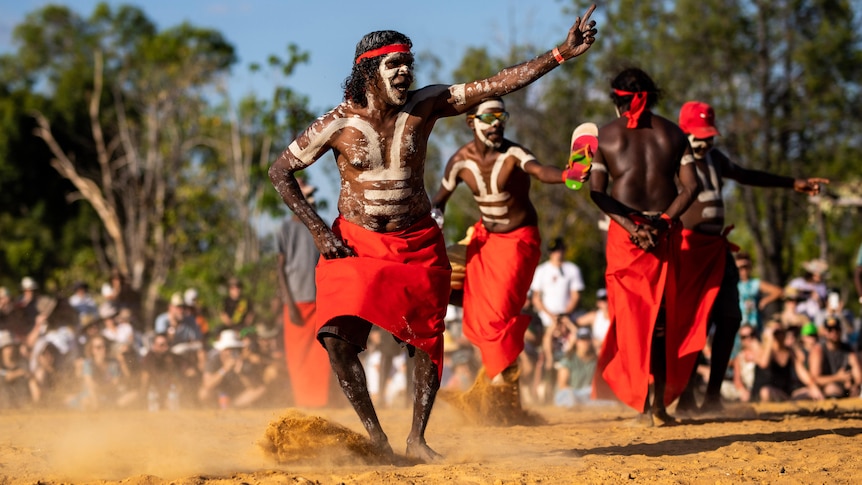 Aboriginal Dancers dance on sand. 
