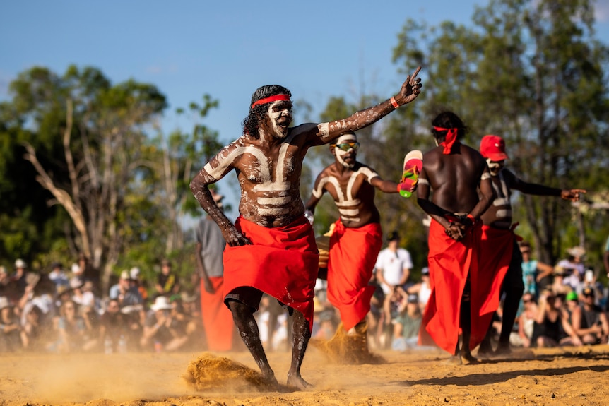Aboriginal Dancers dance on sand. 