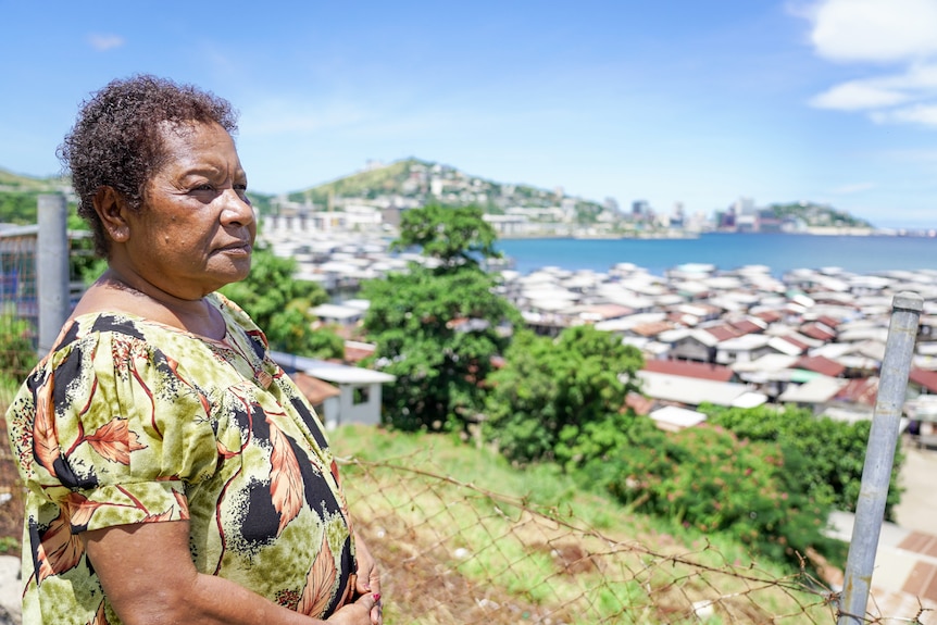 A Papua New Guinean woman with cropped dark hair looks out at Port Moresby from a hill 