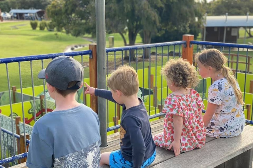 Four children sitting on a bench overlooking a park.