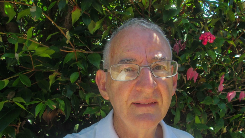 71-year-old Ron Smith wearing glasses, standing in front of green hedge.