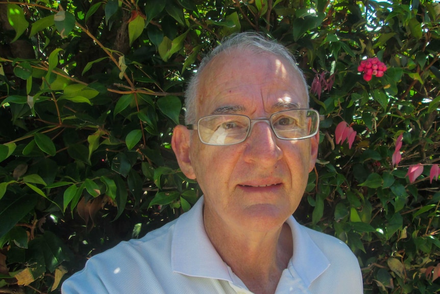 71-year-old Ron Smith wearing glasses, standing in front of green hedge.