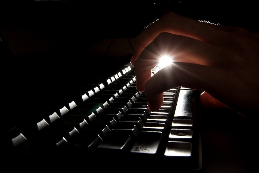 A backlit hand types on a computer keyboard.