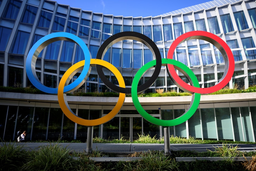 The Oympic rings in front of a building. 