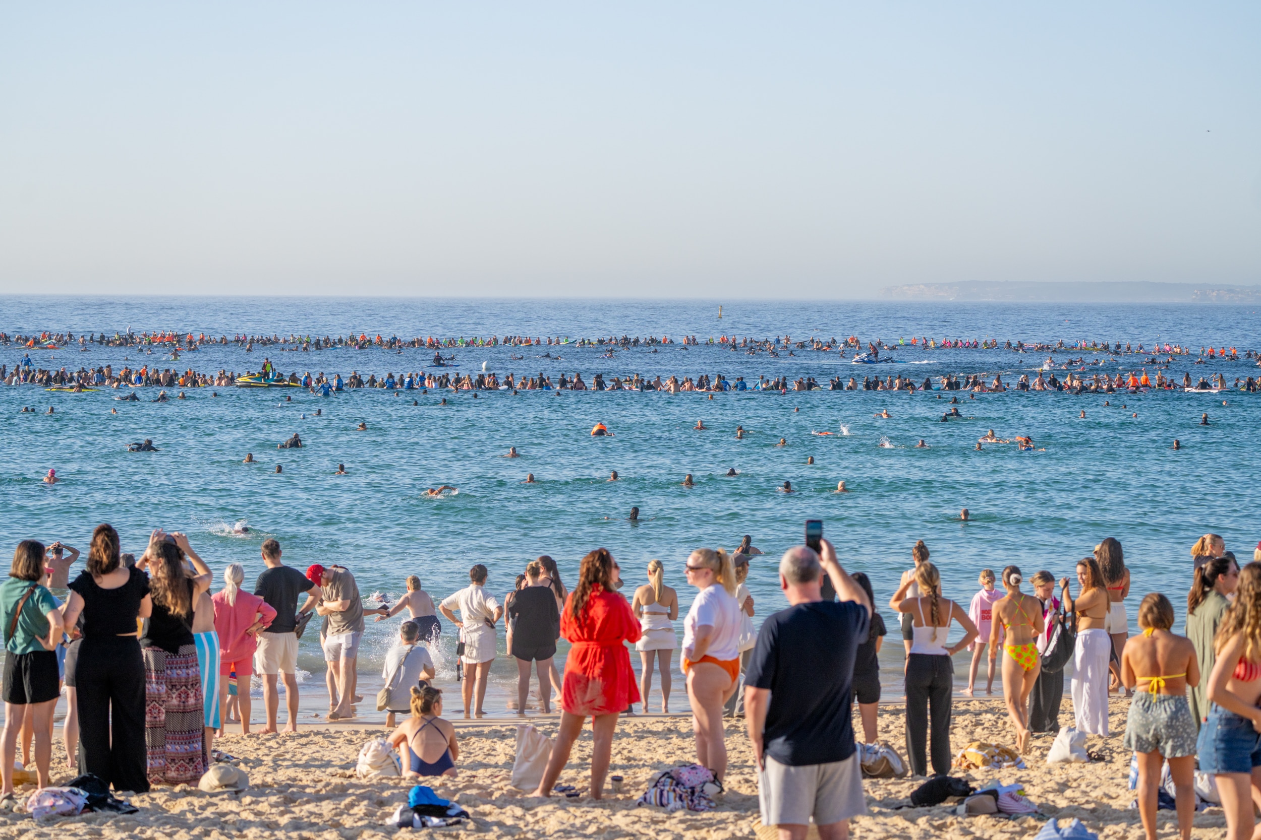 La gente parada en la orilla observa a la gente formar un círculo sobre tablas en el mar