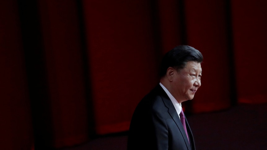 Chinese President Xi Jinping stands in a darkened room, as if he was about to make a speech