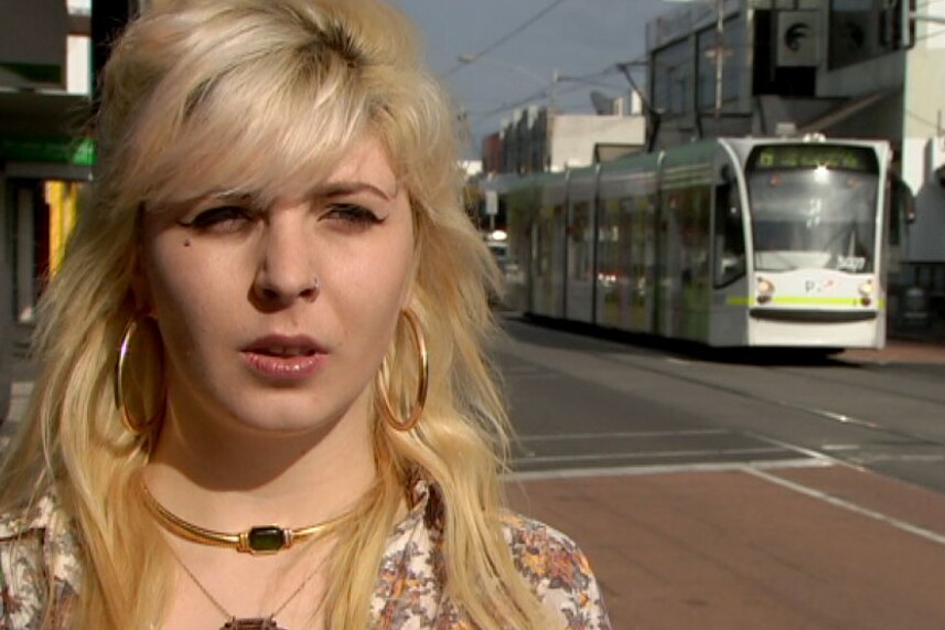 India Rose standing on a footpath with a tram over her right shoulder.