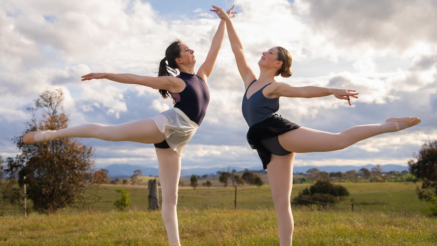 Two ballet dancers posed on a hill.