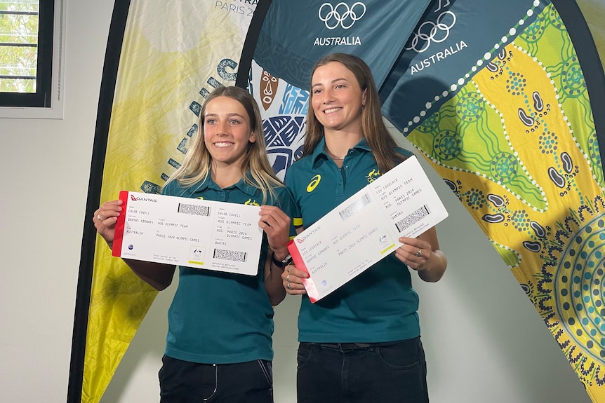 Two young women skateboarders with giant plane tickets in Australian olympic team gear