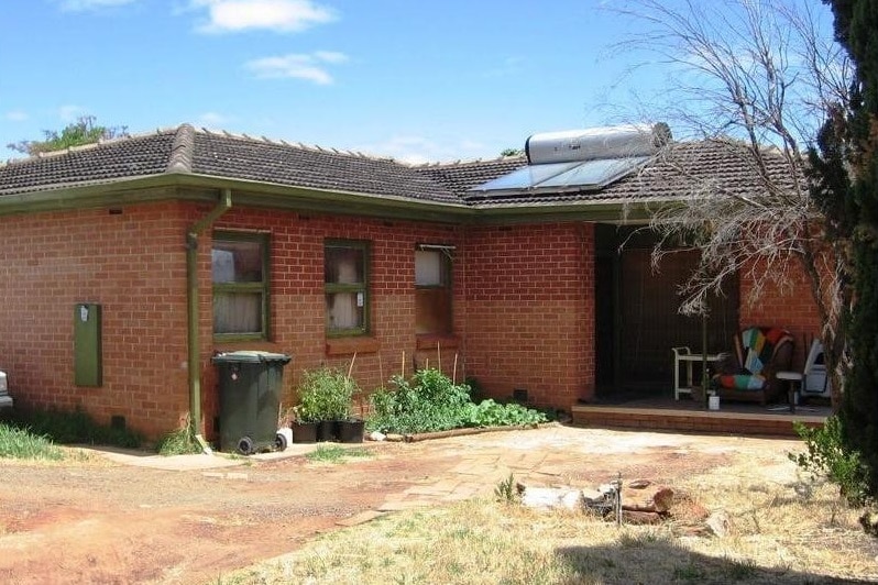 A red brick house with dry lawn and a bin outside
