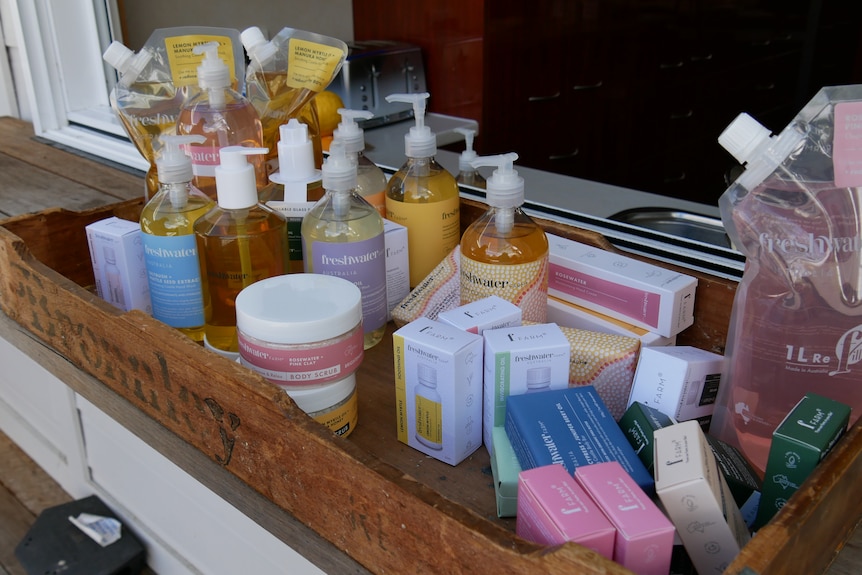 Un montón de productos en una bandeja que incluyen: barras de jabón, aceites esenciales, cremas para manos, exfoliantes corporales, lavado de manos.